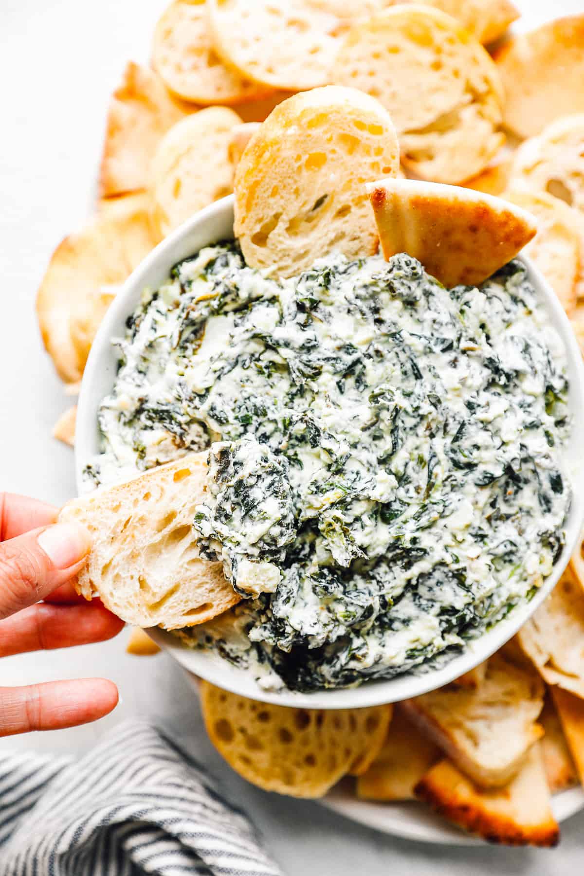 crockpot spinach dip in a white bowl with dippers