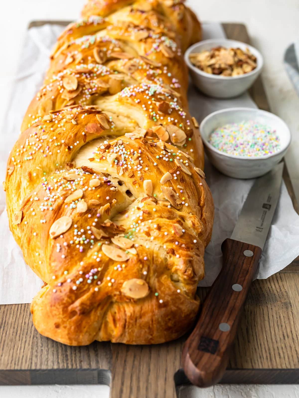 loaf of sweet bread on cutting board with small bowls of almonds and sprinkles
