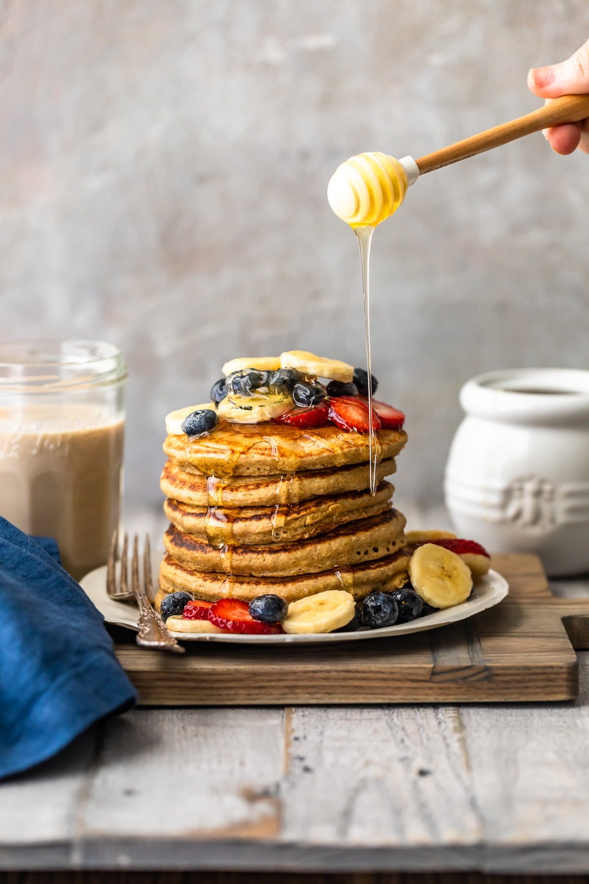 pouring honey on easy blender banana pancakes with fresh fruit