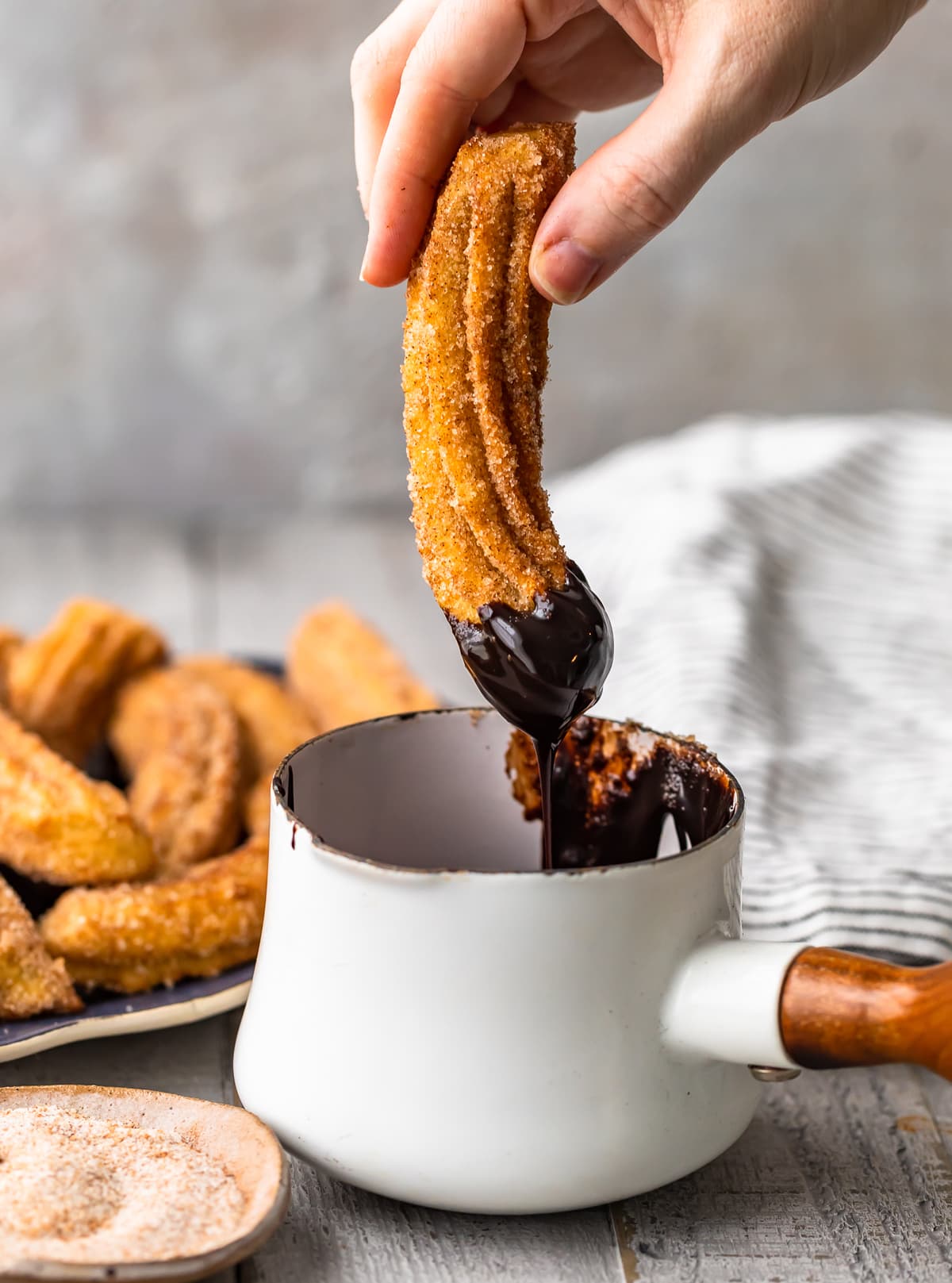 hand dipping a homemade churro into a pot of melted chocolate.