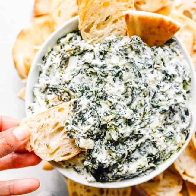 crockpot spinach dip in a white bowl with dippers