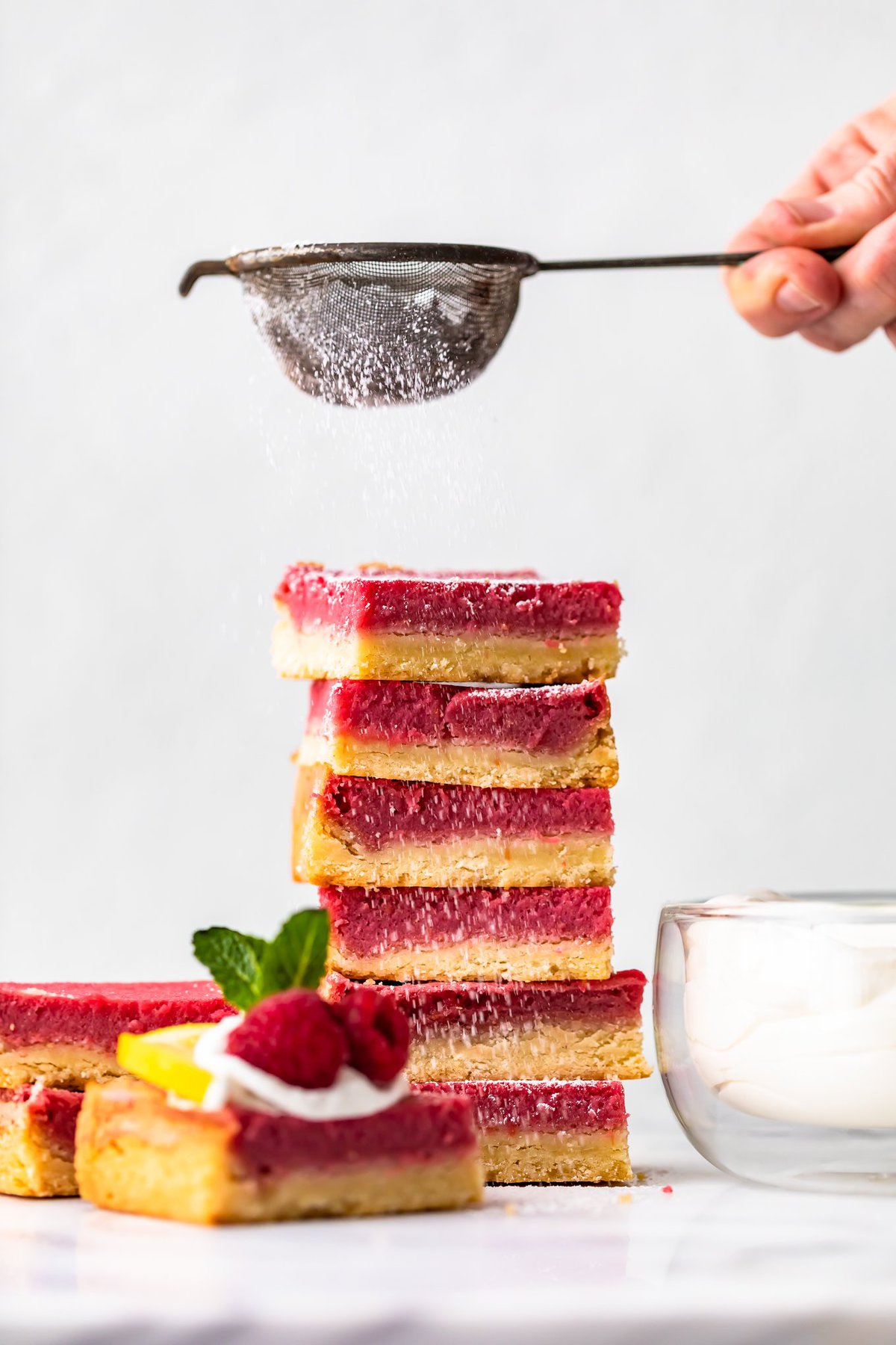 sprinkling powdered sugar over a stack of raspberry bars