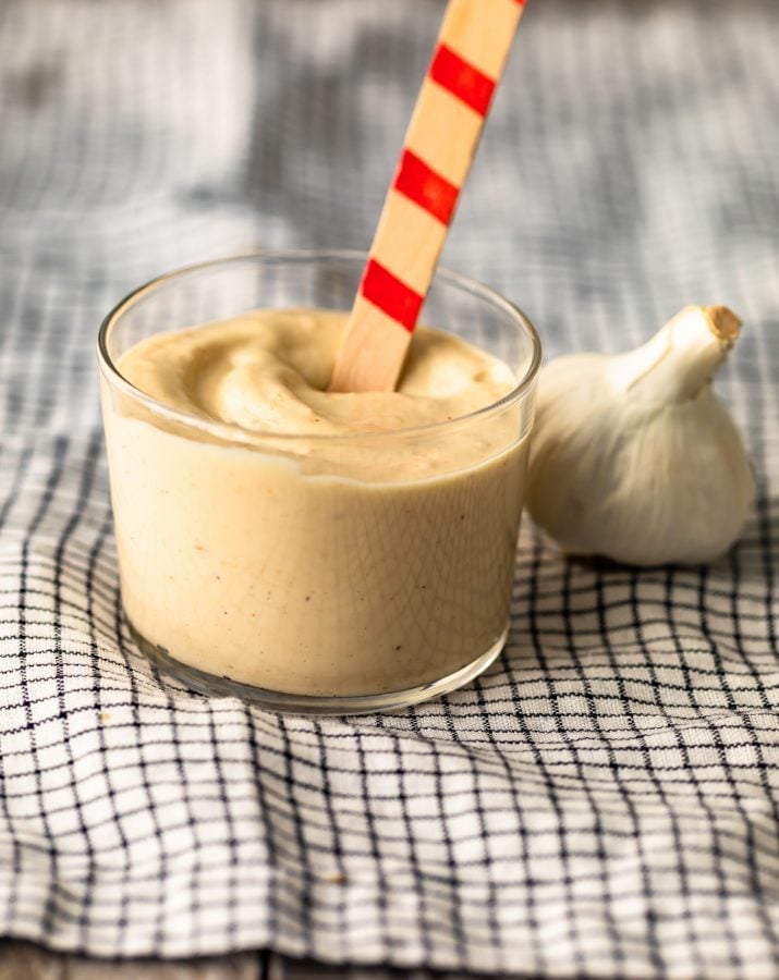 a container of aioli next to a head of garlic