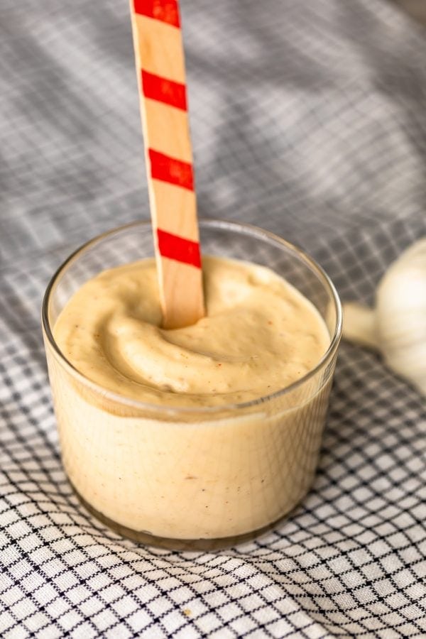 small glass bowl full of creamy aioli, with a red-striped wooden stick