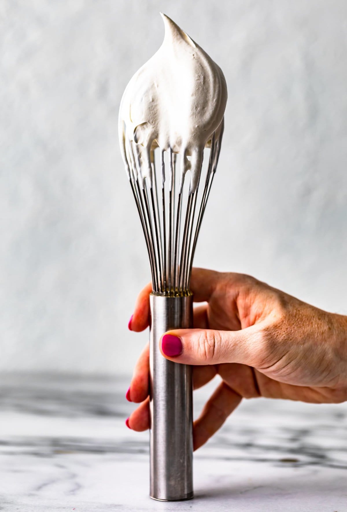 hand holding a whisk dipped in whipped cream