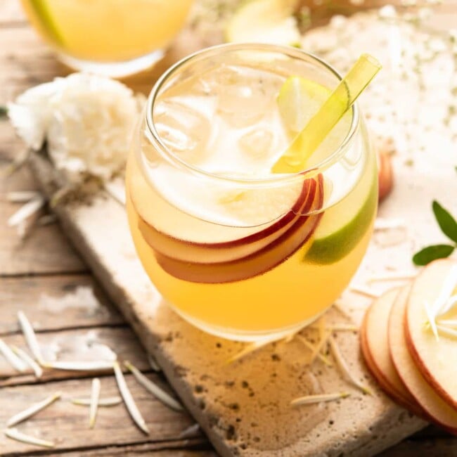 A refreshing apple pie drink garnished with slices of apples and sprigs of thyme.