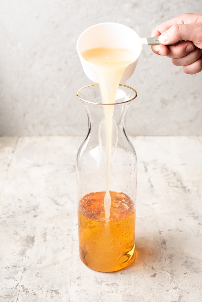 Pouring peach nectar into a pitcher for Apple Pie Drink.