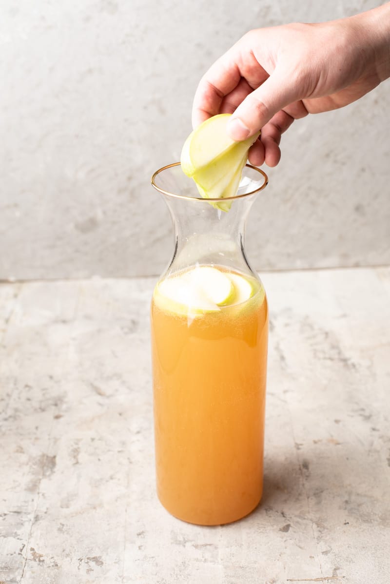 Adding apple slices to a vodka apple drink.