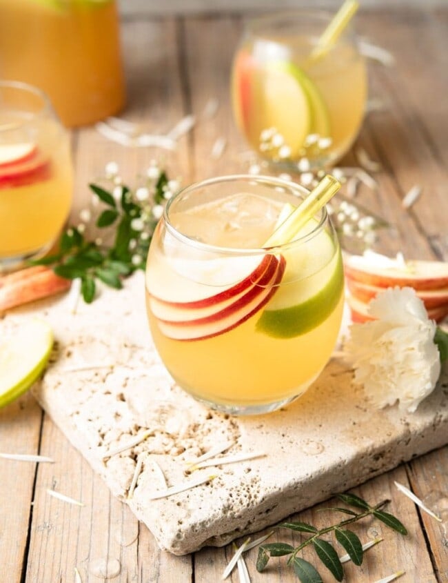An apple pie drink in a round glass with slices of apple and a straw