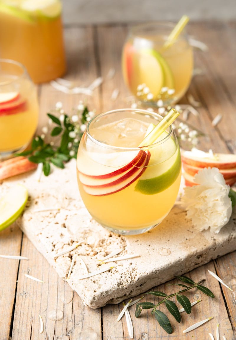 An apple pie drink in a round glass with slices of apple and a straw