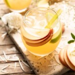 An apple pie drink in a round glass with slices of apple and a straw