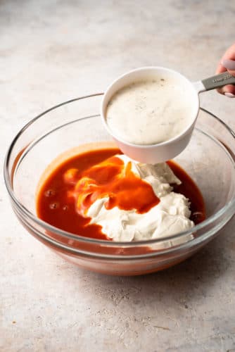 A person pouring buffalo chicken dip sauce into a bowl.