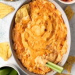 buffalo chicken dip in white baking dish with celery stalk dipped in it