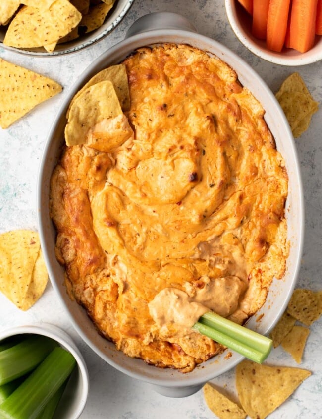buffalo chicken dip in white baking dish with celery stalk dipped in it
