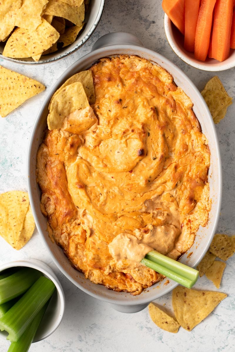 An overhead shot of buffalo chicken dip in a dish with celery sticks and chips around it