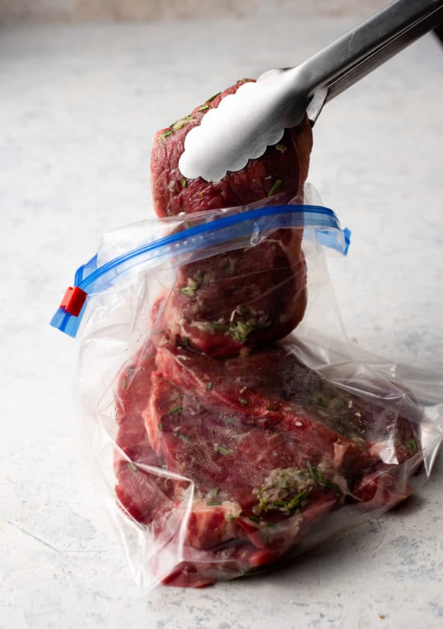 A new york strip steak is being cut out of a plastic bag using a knife.