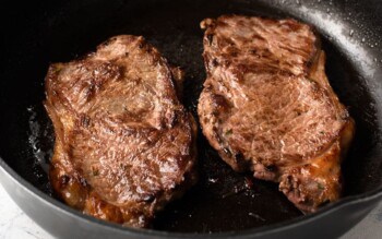 New York strip steaks are being cooked in a cast iron skillet.