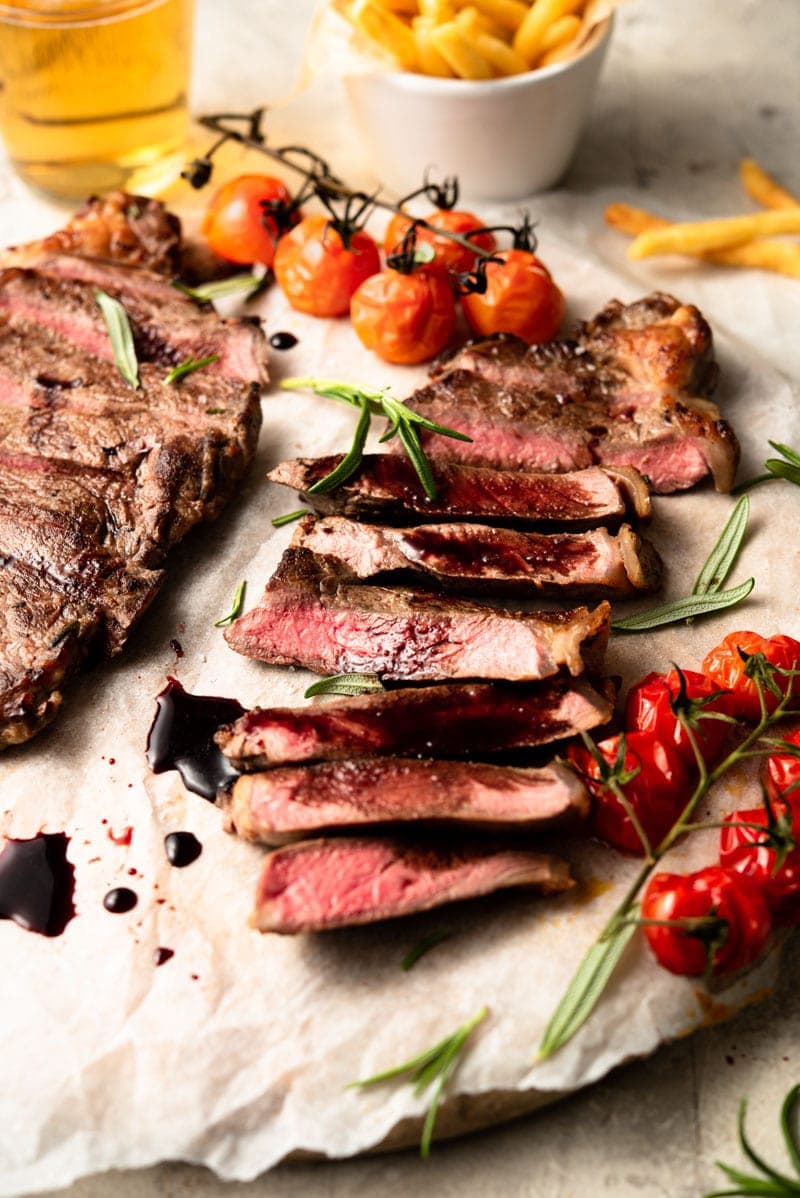 sliced new york strip steak on parchment paper with tomatoes and balsamic glaze.