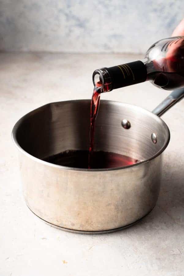 a person pouring red wine into a pan, adding a sprinkle of salt.