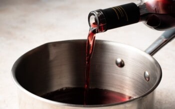 a person pouring red wine into a pan, adding a sprinkle of salt.
