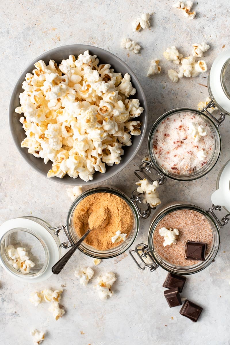 over the top shot of popcorn in a bowl surrounded by different powdered ingredients in jars