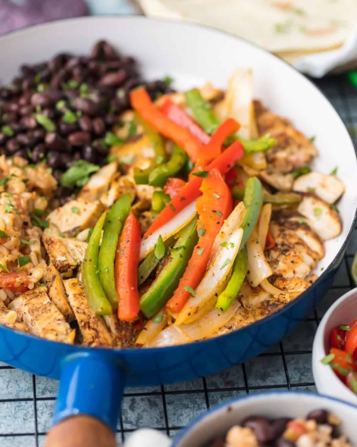 This easy Chicken Fajitas recipe has quickly become a favorite around here. AQueso Smothered Chicken Fajita Recipe with all the best ingredients! Chicken and veggies in a blue skillet.