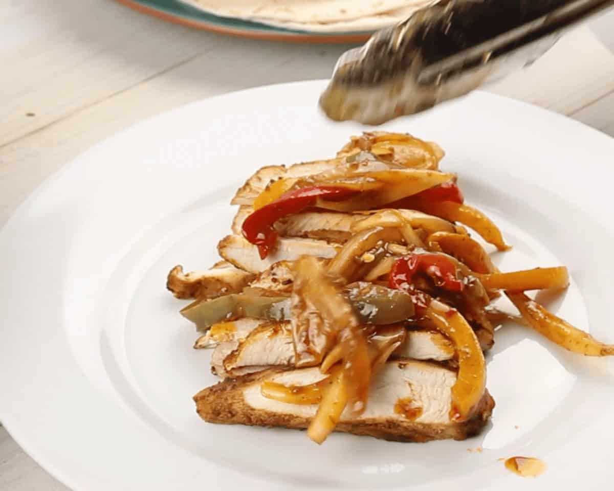 Chicken layered with veggies on a white plate.