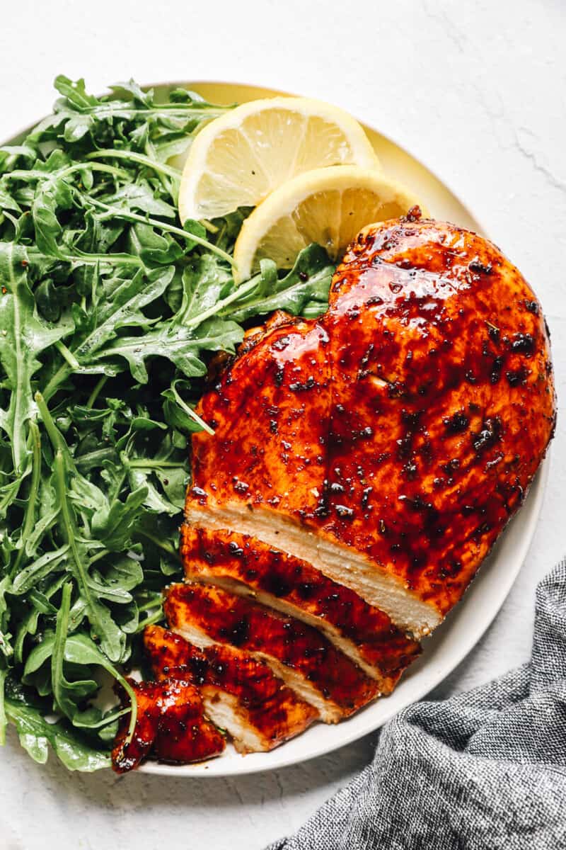 sliced balsamic chicken on white plate with simple salad and lemon