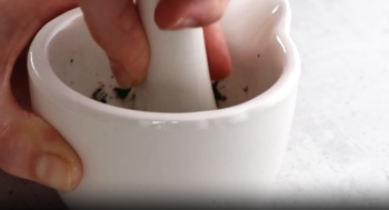 a hand grinding herbs in a white mortar and pestle.