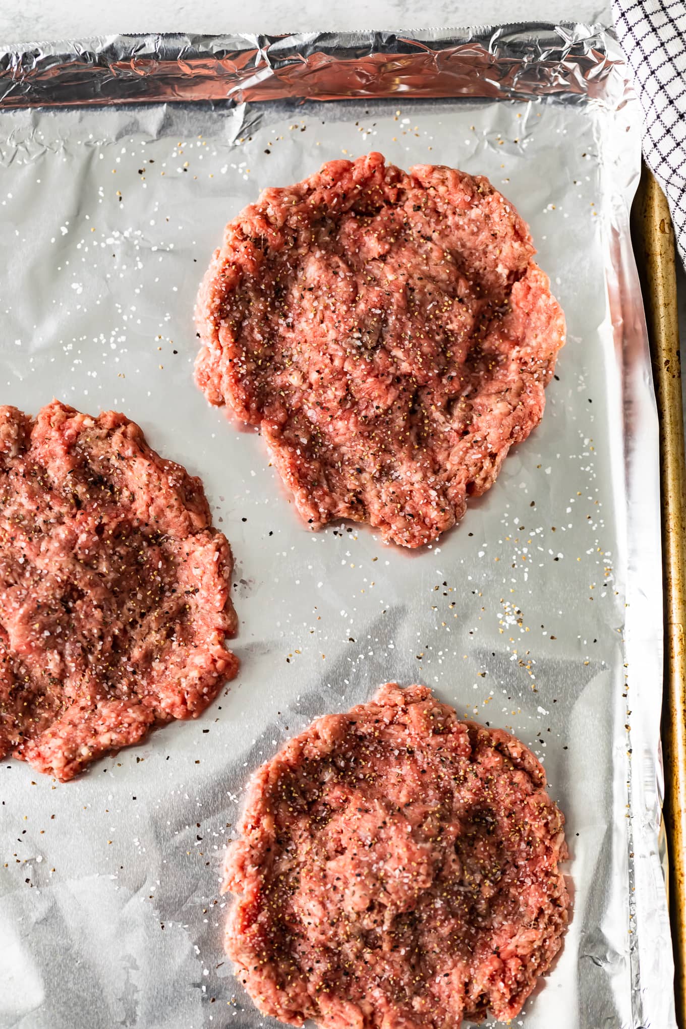 uncooked ground beef burger patties on a baking sheet