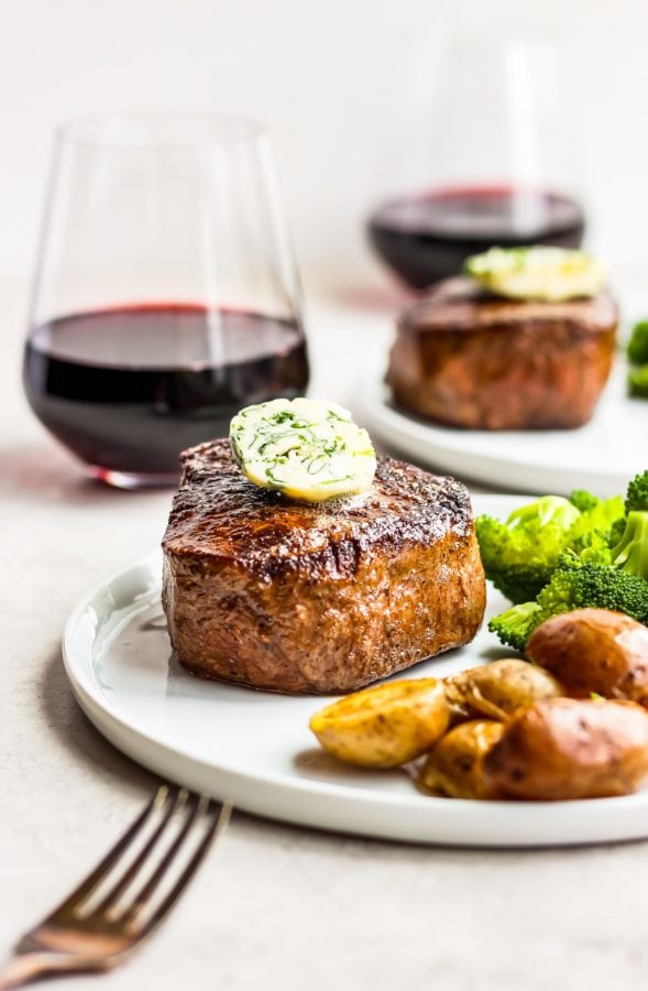 two plates of steak with two glasses of red wine
