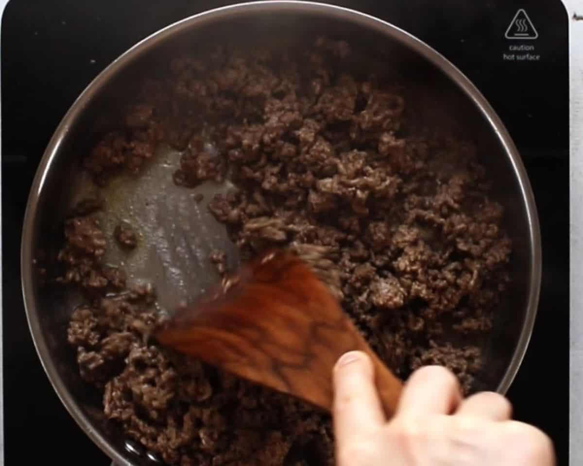 Cooking the ground beef in a pan with a wooden spoon.