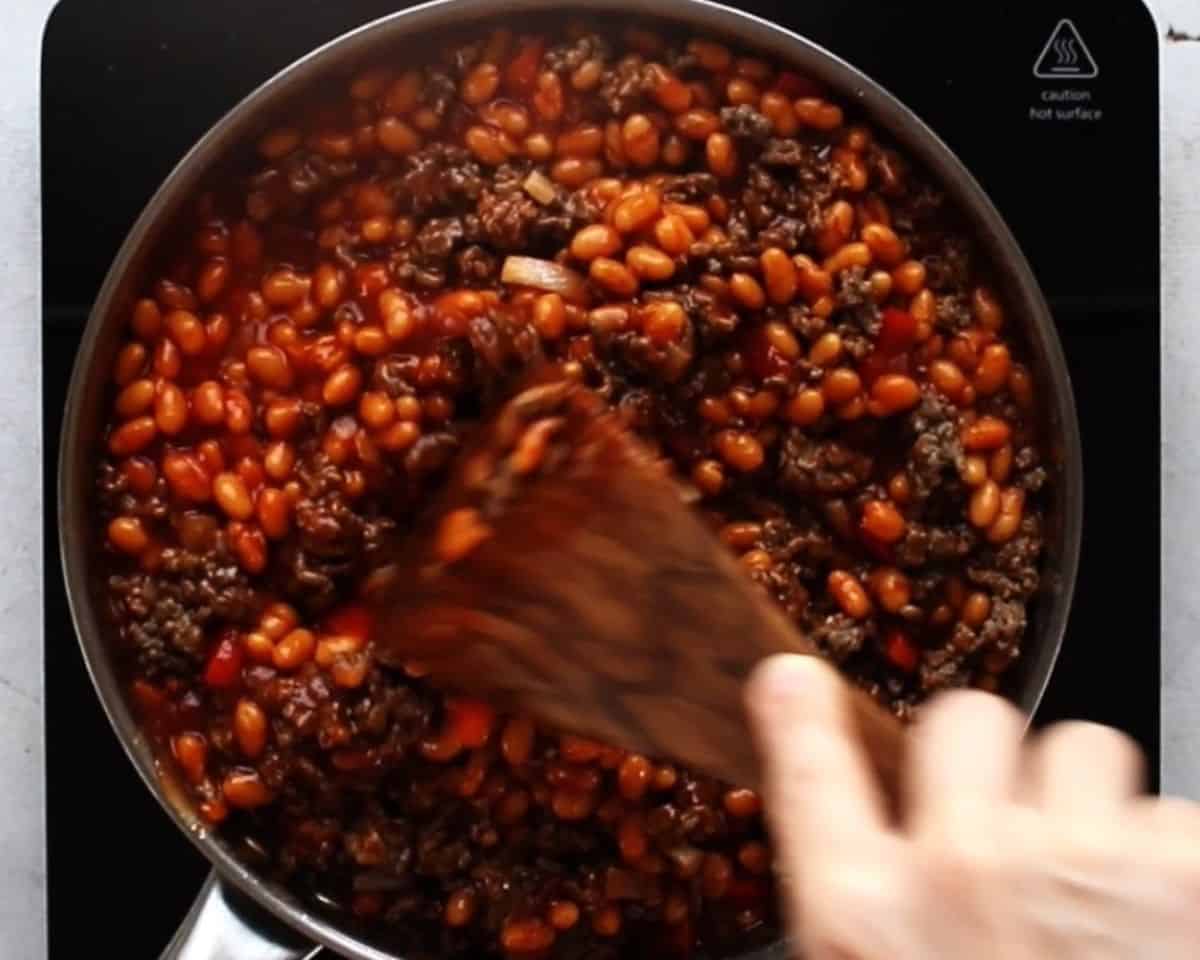 Stirring all the ingredients in BBQ baked beans in a pan with a wooden spoon.