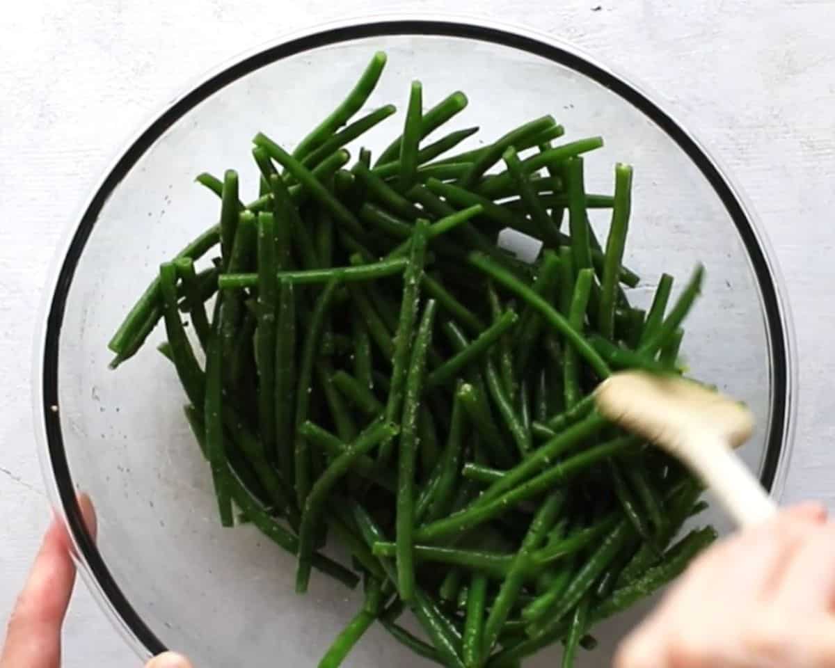 Stirring green beans seasoned with salt, pepper, and olive oil.