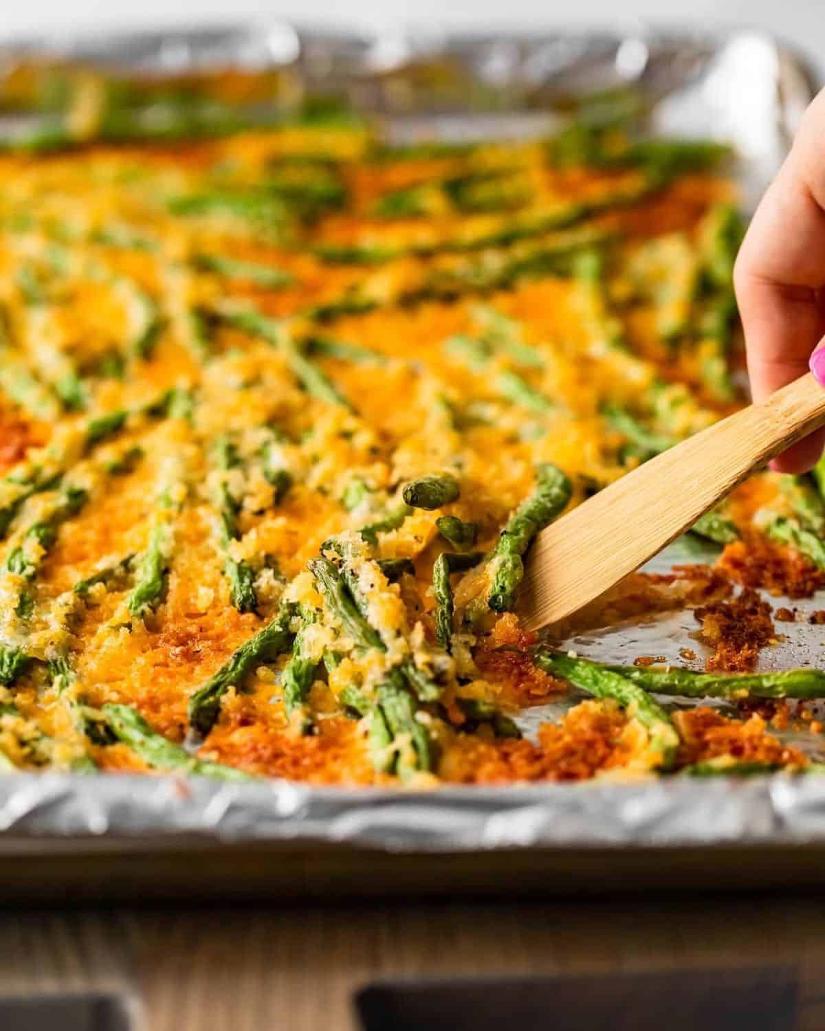 A wooden spatula scooping up the crispy baked green beans.