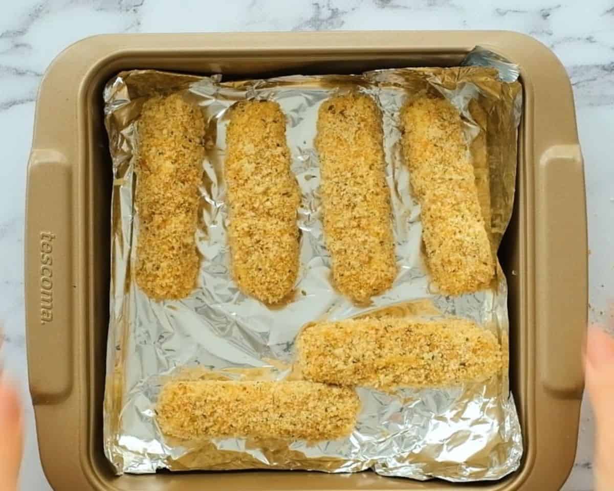 Breaded mozzarella sticks in an aluminum foil lined pan.