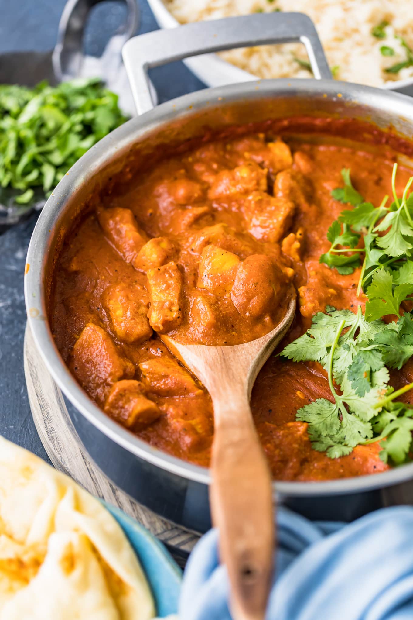close up view of chicken curry in pan with wooden spoon
