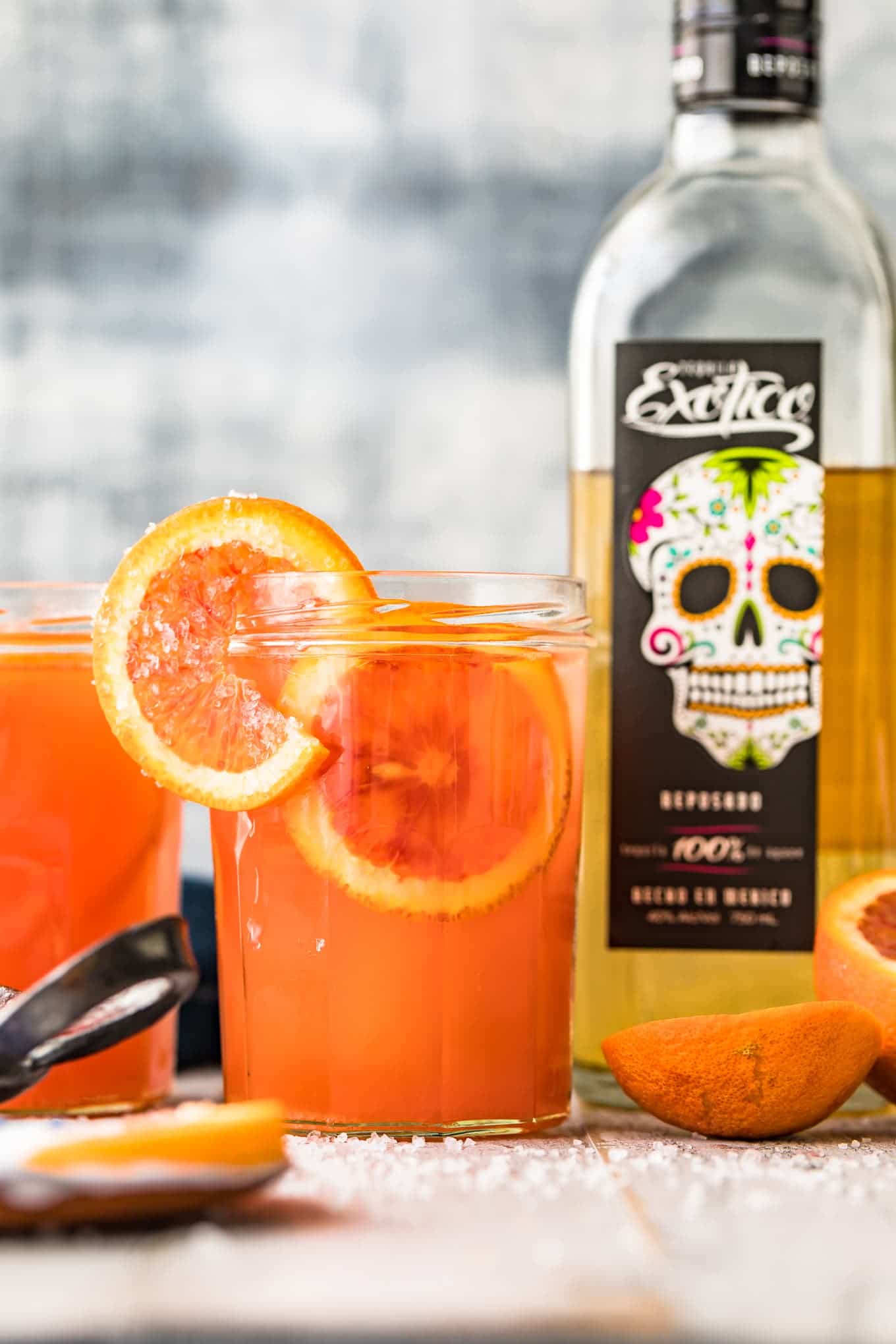 A blood orange paloma cocktail in front of a bottle of tequila