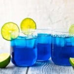 three blue margaritas in glasses topped with sliced limes