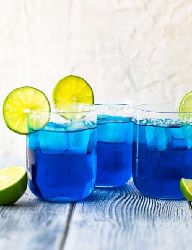 three blue margaritas in glasses topped with sliced limes