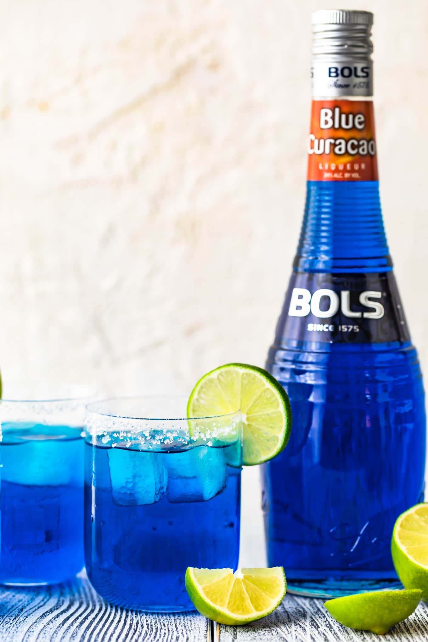 A blue margarita cocktail with a bottle of blue curacao in the background