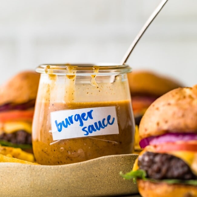 burger sauce in a cup with a spoon and burgers beside it