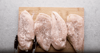 Four caesar chicken breasts on a cutting board with a knife.