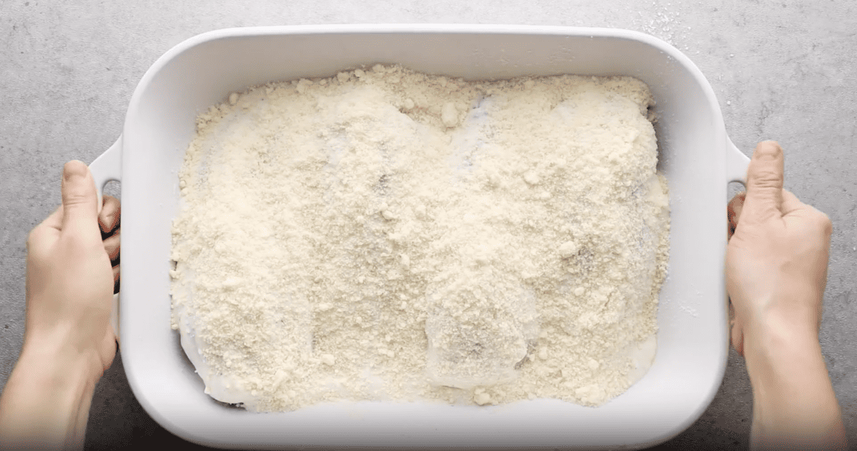 A person holding a baking dish filled with caesar chicken and breadcrumbs.