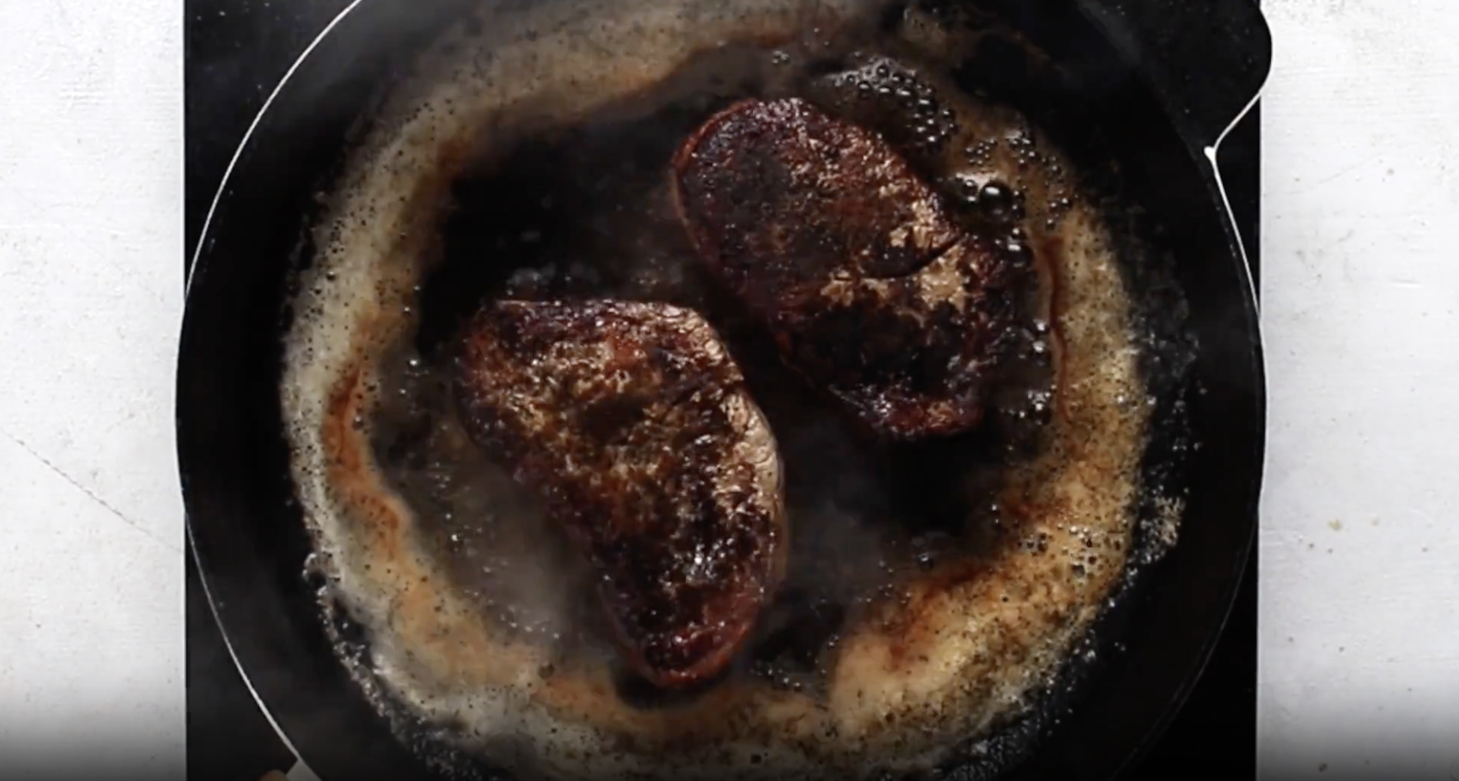 2 filet mignon searing in a cast iron skillet.