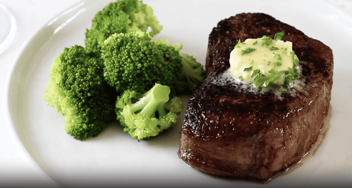 filet mignon topped with cilantro steak butter and served with a side of broccoli on a white plate.