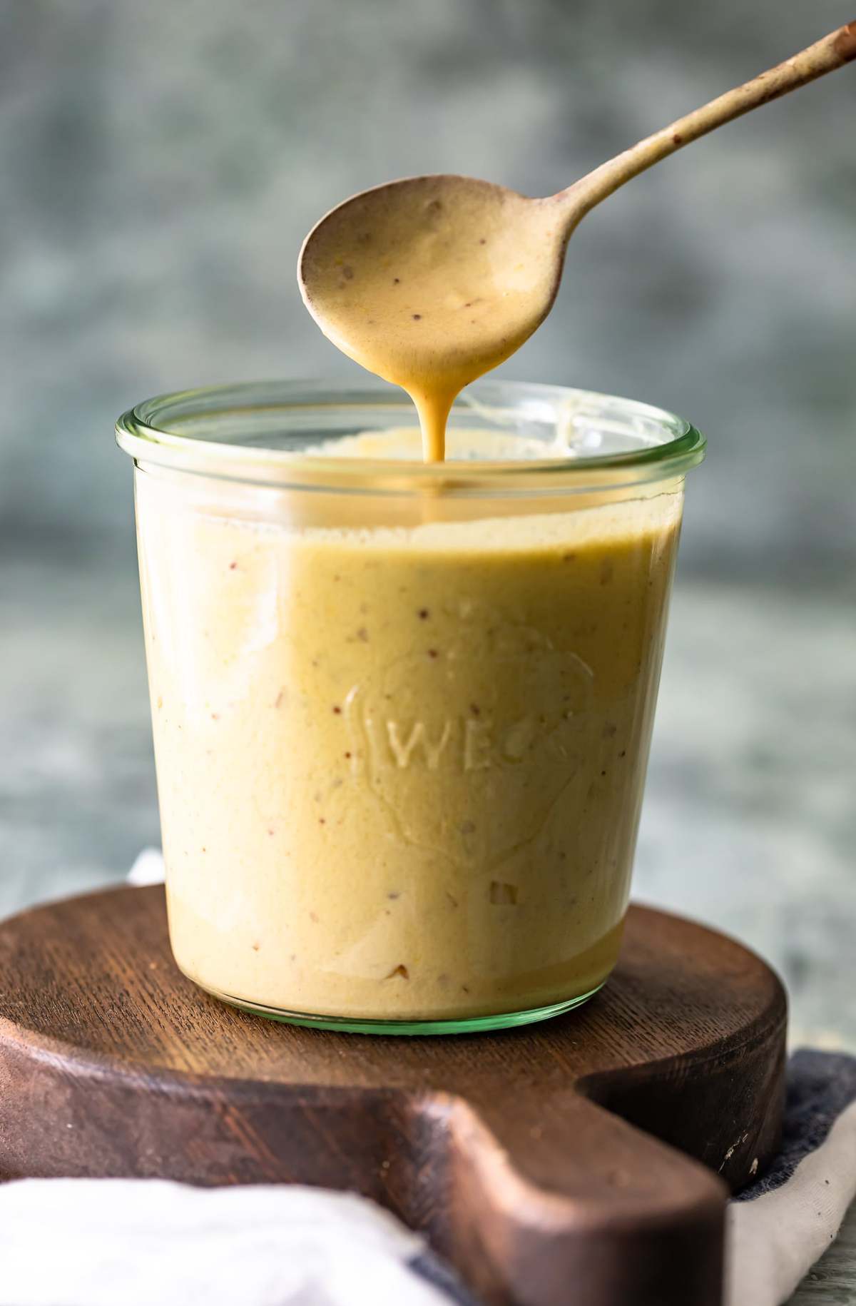 A spoon dripping mustard cream sauce into a jar