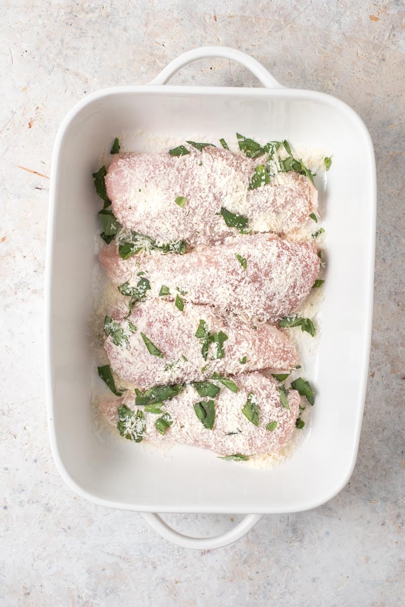 An overhead shot of chicken coated in parmesan in a casserole dish 