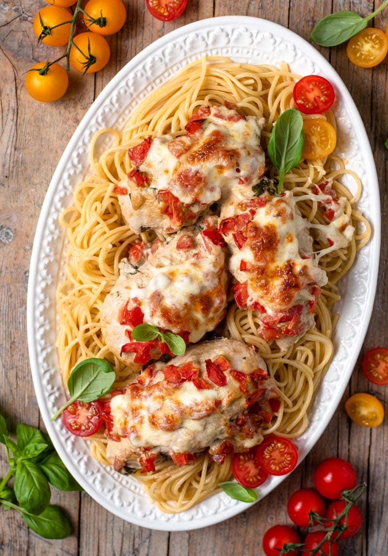 An overhead shot of cheesy bruschetta chicken on a serving plate with spaghetti