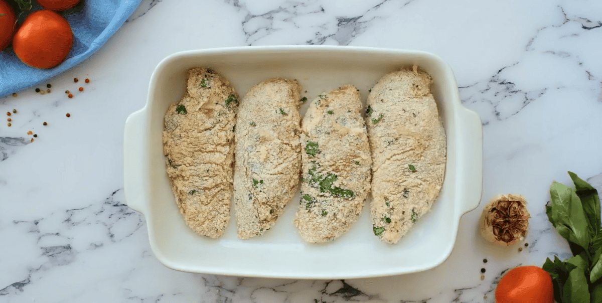 Parmesan coated chicken in a white baking dish.